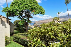 A residential area with a large tree, manicured lawns, and a view of a hilly landscape with wind turbines. - Kihei Holiday 215 (Kihei)