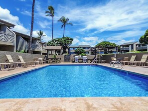 A swimming pool with lounge chairs and a covered seating area, surrounded by buildings with a tropical architectural style. - Kihei Holiday 215 (Kihei)