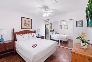 A hotel room with a bed, bedside tables, a mirror, and a ceiling fan. - Kihei Holiday 215 (Kihei)