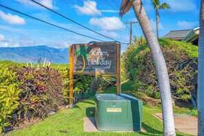 Ein Schild mit der Aufschrift 'Kihei Holiday', im Hintergrund sind Berge zu sehen.