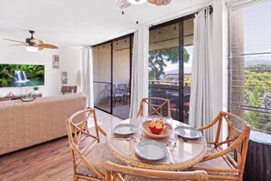 A dining area with a round table, chairs, and a view of the outdoors. - Kihei Holiday 215 (Kihei)