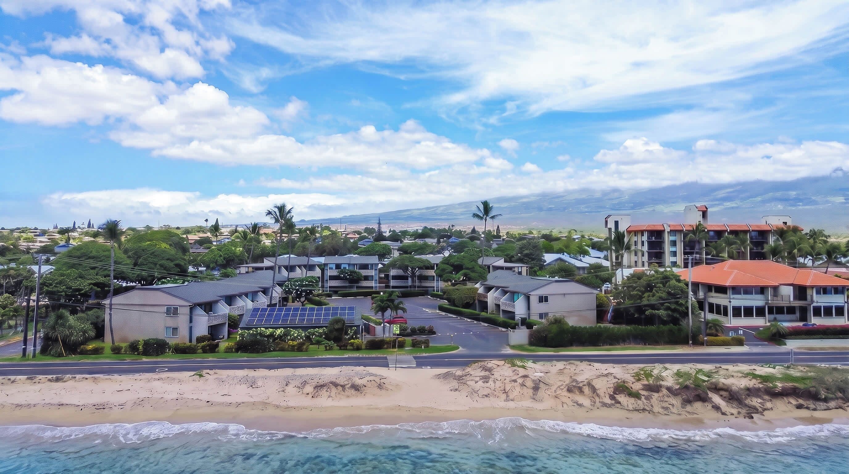A coastal residential area with buildings, a beach, and a mountain in the background.