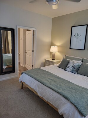 A bedroom with a bed, bedside table, lamp, framed artwork, and a door leading to another room. - Coastal Retreat w/Resort Pools & Shuttle to Beach (Millville)