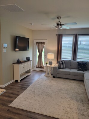 A living room with a TV, a ceiling fan, a sofa, a coffee table, and a door with curtains. - Coastal Retreat w/Resort Pools & Shuttle to Beach (Millville)