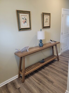 Une console en bois, ornée d’une lampe et de quelques canards décoratifs, est placée entre deux tableaux encadrés qui décorent un mur sobre.