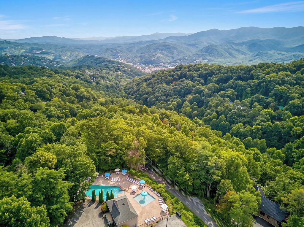 An aerial view of a resort with a swimming pool, lounge chairs, and a road leading to a mountain town.