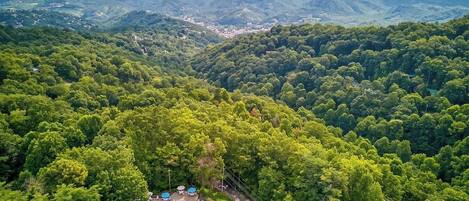 An aerial view of a resort with a swimming pool, lounge chairs, and a road leading to a mountain town.