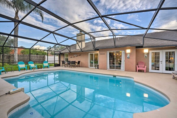 Une piscine extérieure couverte, dotée d’un toit en verre, entourée de chaises et bordée d’un bâtiment avec un patio.