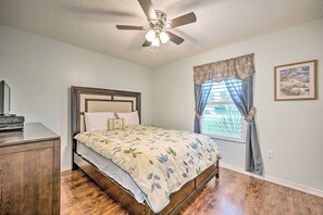 A bedroom with a bed, a ceiling fan, a window with curtains, a bedside table, and a framed picture on the wall. - Phenomenal 3-bedroom house with AC in charming Kissimmee w/heated pool & lanai (Kissimmee)
