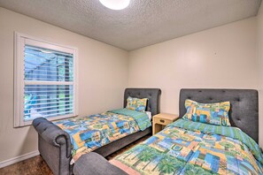 Ein Schlafzimmer mit zwei Betten, einem Fenster mit Jalousien, einer Deckenleuchte und einem kleinen Nachttisch.