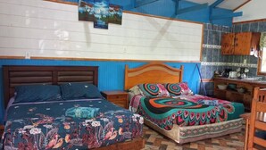 Una habitación con dos camas, cabecero de madera, piso de baldosas y una zona de cocina con armarios y un lavamanos.