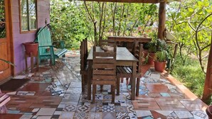 Un espacio de patio cubierto con una mesa y sillas de madera, rodeado de plantas en macetas y un suelo de baldosas.