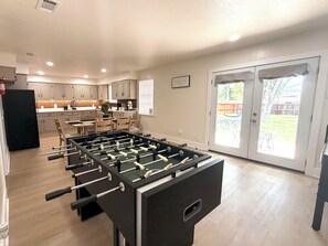 A modern kitchen with a foosball table, a dining area with chairs, and a view of the backyard through glass doors. - 4BR Home Perfect for State Fair of TX (Dallas)