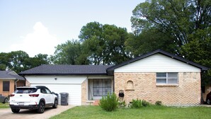 Uma casa térrea com garagem, fachada de tijolos e um pequeno jardim frontal.