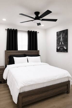 Ein Schlafzimmer mit einem Bett, einem Deckenventilator, schwarzen Vorhängen, einem Fenster und einem Bild vom Eiffelturm.