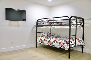 Un lit superposé avec une couvre-lit à motifs, un téléviseur à écran plat fixé au mur et un plancher en bois de couleur claire.