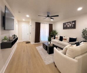 A modern living room with a flat-screen TV, a ceiling fan, a sofa, and a coffee table. - 4BR Home Perfect for State Fair of TX (Dallas)
