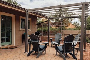 Un espace extérieur aménagé avec des chaises Adirondack, une pergola et un barbecue.