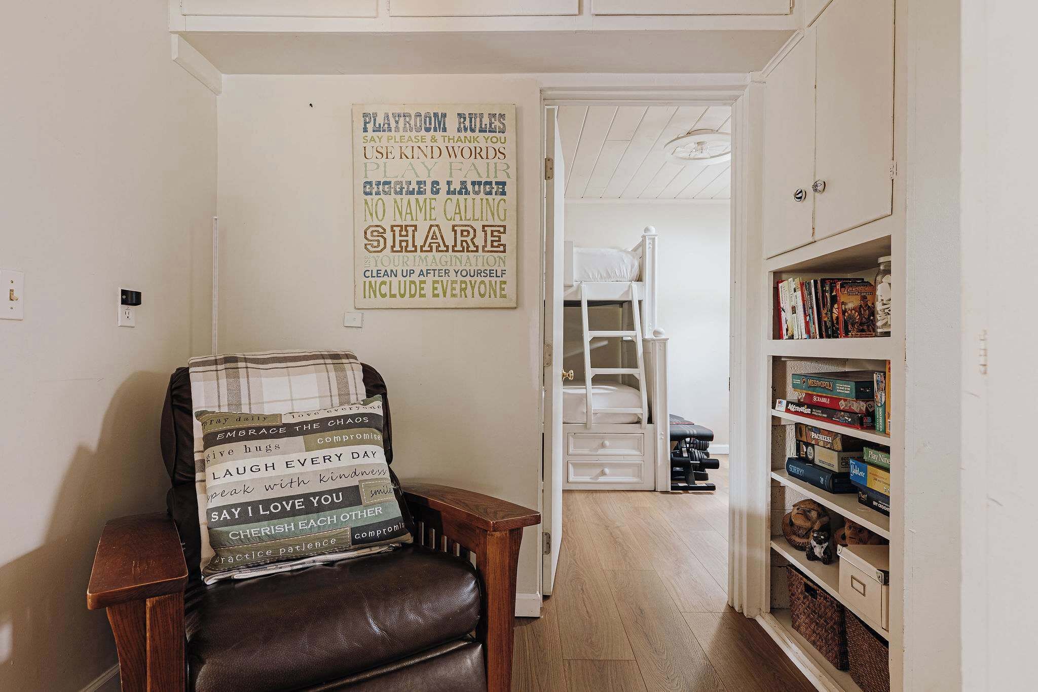 A cozy room with a chair adorned with motivational phrases, a bookshelf filled with games, and a door leading to another room.