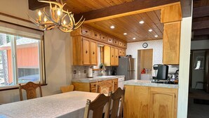 Una cucina con mobili in legno, un tavolo da pranzo con sedie, un lampadario e un frigorifero.