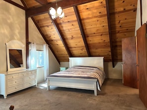 Ein Schlafzimmer mit schrägem Dach, einem Bett, einer Kommode, einem Spiegel und einer Tür.