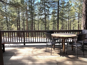 Eine Holzterrasse mit einem runden Tisch und Stühlen, umgeben von hohen Kiefern.
