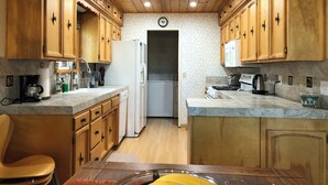 Una cucina con mobili in legno, un frigorifero, un fornello e una sveglia appesa al muro.