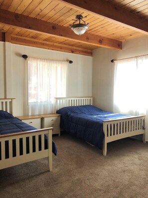 Habitación con dos camas individuales, techo de madera y ventana con cortinas traslúcidas.