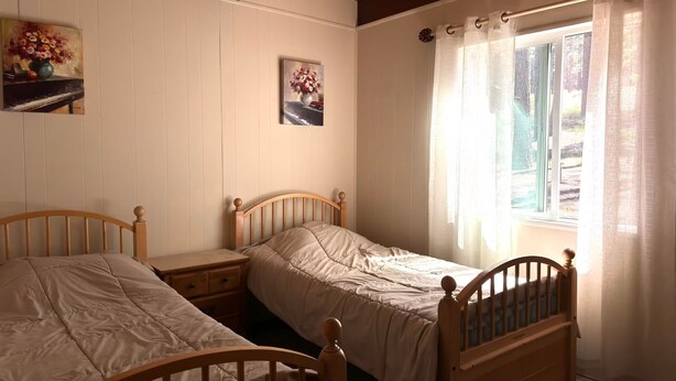 Una camera da letto con due letti in legno, un comodino, una finestra con tende e due quadri appesi al muro.