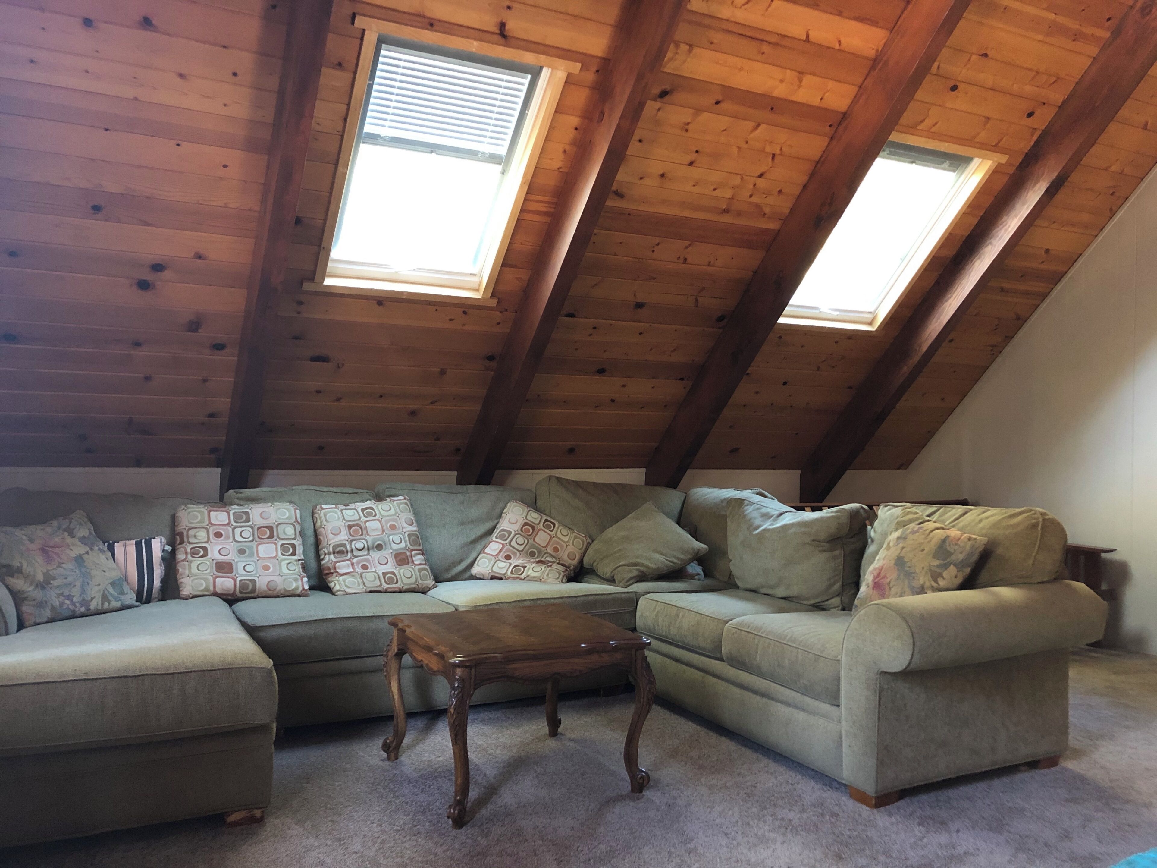Un loft con techo de madera, un sofá seccional y una pequeña mesa de madera.