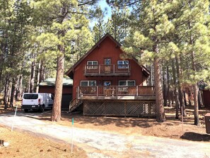 A two-story cabin with a balcony, surrounded by pine trees. - 3-bedroom cabin in gorgeous South Lake Tahoe with AC (South Lake Tahoe)