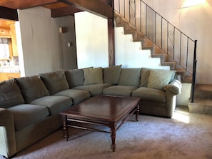 Ein Wohnzimmer mit einer Eckcouch, einem Holztisch und einer Treppe mit Metallgeländer.