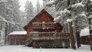 Una baita di legno a due piani con un balcone, circondata da alberi innevati.