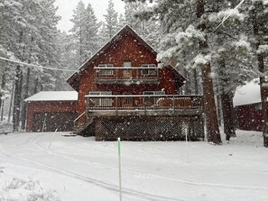 Eine zweistöckige Holzhütte mit Balkon, umgeben von schneebedeckten Bäumen.