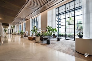 A spacious lobby with large windows, modern furniture, and potted plants. - Cozy Miami Studio | Pool & Gym | City Views (Miami)
