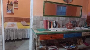 A room with a bed, a wooden desk with a mirror, and a shelf with various items. - Rustic house with all the charm of the coast. (Maraú)