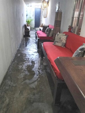 A narrow hallway with a wet floor, a red sofa with patterned cushions, and a wooden bench. - Rustic house with all the charm of the coast. (Maraú)