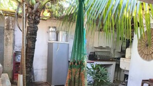 A rustic outdoor kitchen area with a hanging hammock, a refrigerator, and a potted plant. - Rustic house with all the charm of the coast. (Maraú)