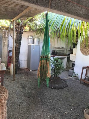 A rustic outdoor kitchen area with a hanging hammock, a refrigerator, and a potted plant. - Rustic house with all the charm of the coast. (Maraú)