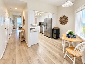 A modern kitchen with a central island, stainless steel appliances, and a dining area with a view. - Coastal Luxury at Surf Club | Direct Oceanfront | Resort-Style Amenities (Palm Coast)