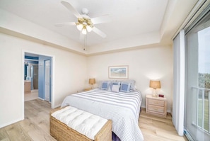 A bedroom with a bed, a nightstand, a lamp, a ceiling fan, and a window. - Coastal Luxury at Surf Club | Direct Oceanfront | Resort-Style Amenities (Palm Coast)