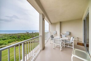 Een balkon met uitzicht op zee, wit meubilair en een glazen deur.
