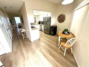 A modern kitchen with a central island, stainless steel appliances, and a dining area with a wooden table and white chairs. - Coastal Luxury at Surf Club | Direct Oceanfront | Resort-Style Amenities (Palm Coast)