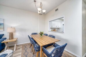 A dining area with a wooden table, blue wicker chairs, a hanging light fixture, and a wall-mounted mirror. - Coastal Luxury at Surf Club | Direct Oceanfront | Resort-Style Amenities (Palm Coast)