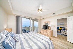 A bedroom with a bed, a TV, a dresser, and a balcony with a view. - Coastal Luxury at Surf Club | Direct Oceanfront | Resort-Style Amenities (Palm Coast)