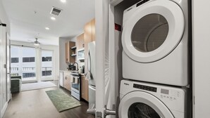 A laundry room with stacked washers and dryers, a kitchen area, and a view through a glass door to a balcony. - Modern West Midtown Retreat -Balcony + Pool + Gym (Atlanta)