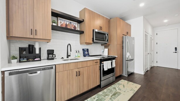 A modern kitchen with wooden cabinets, stainless steel appliances, and a white countertop. - Modern West Midtown Retreat -Balcony + Pool + Gym (Atlanta)