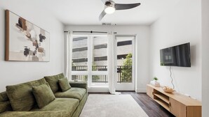 A modern living room with a green sofa, a flat-screen TV, and a ceiling fan. - Modern West Midtown Retreat -Balcony + Pool + Gym (Atlanta)
