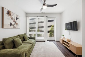 Ein modernes Wohnzimmer mit einem grünen Sofa, einem Flachbildfernseher und einem Deckenventilator.