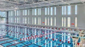 Ein großes Hallenbad mit mehreren Bahnen, hoher Decke und großen Fenstern.